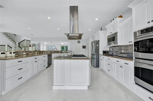 a kitchen with stainless steel appliances kitchen island granite countertop a stove a sink and white cabinets