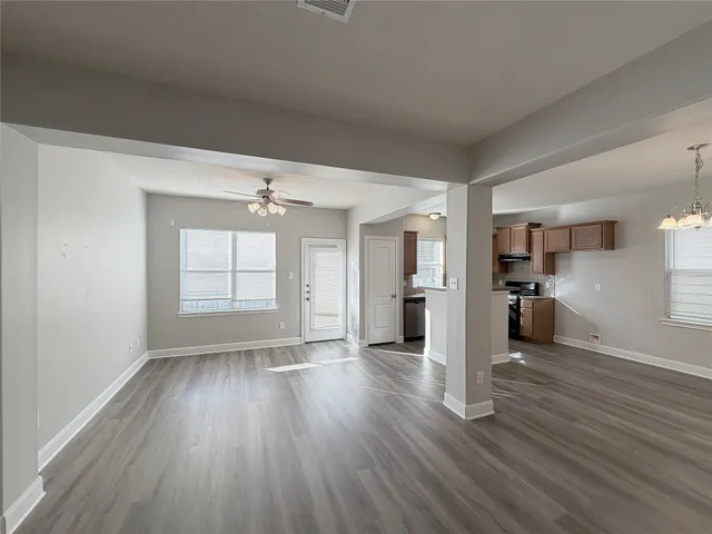 an empty room with wooden floor kitchen view and windows