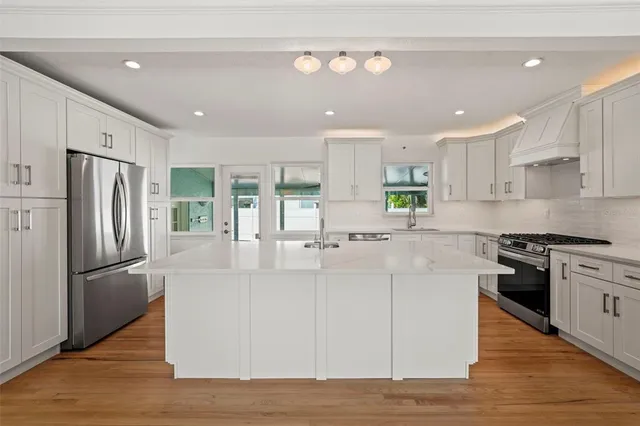 a kitchen with stainless steel appliances granite countertop a refrigerator a sink dishwasher a stove and a refrigerator with wooden floor