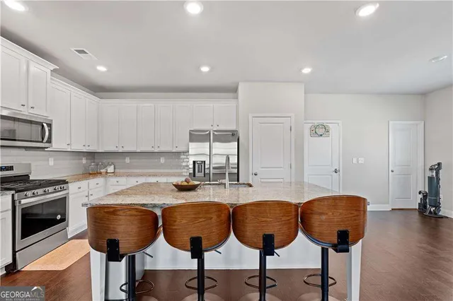 a kitchen with stainless steel appliances granite countertop a stove a sink a refrigerator and white cabinets with wooden floor