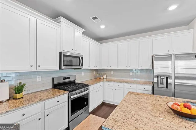a kitchen with granite countertop a sink stainless steel appliances and white cabinets