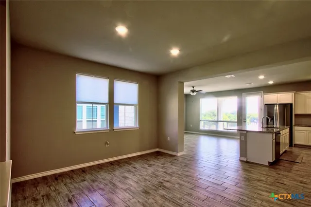 a view of an empty room with wooden floor and a kitchen