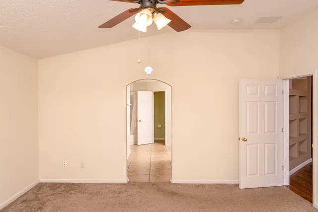 an empty room with a chandelier fan and wooden floor