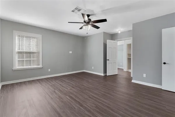 an empty room with wooden floor ceiling fan and windows