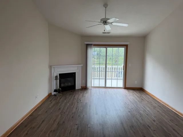 a view of an empty room with wooden floor fireplace and a window