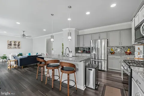 a kitchen with stainless steel appliances granite countertop a refrigerator a stove a sink a dining table and chairs with wooden floor