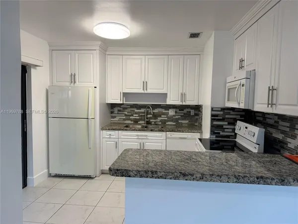 a kitchen with granite countertop a refrigerator sink and cabinets