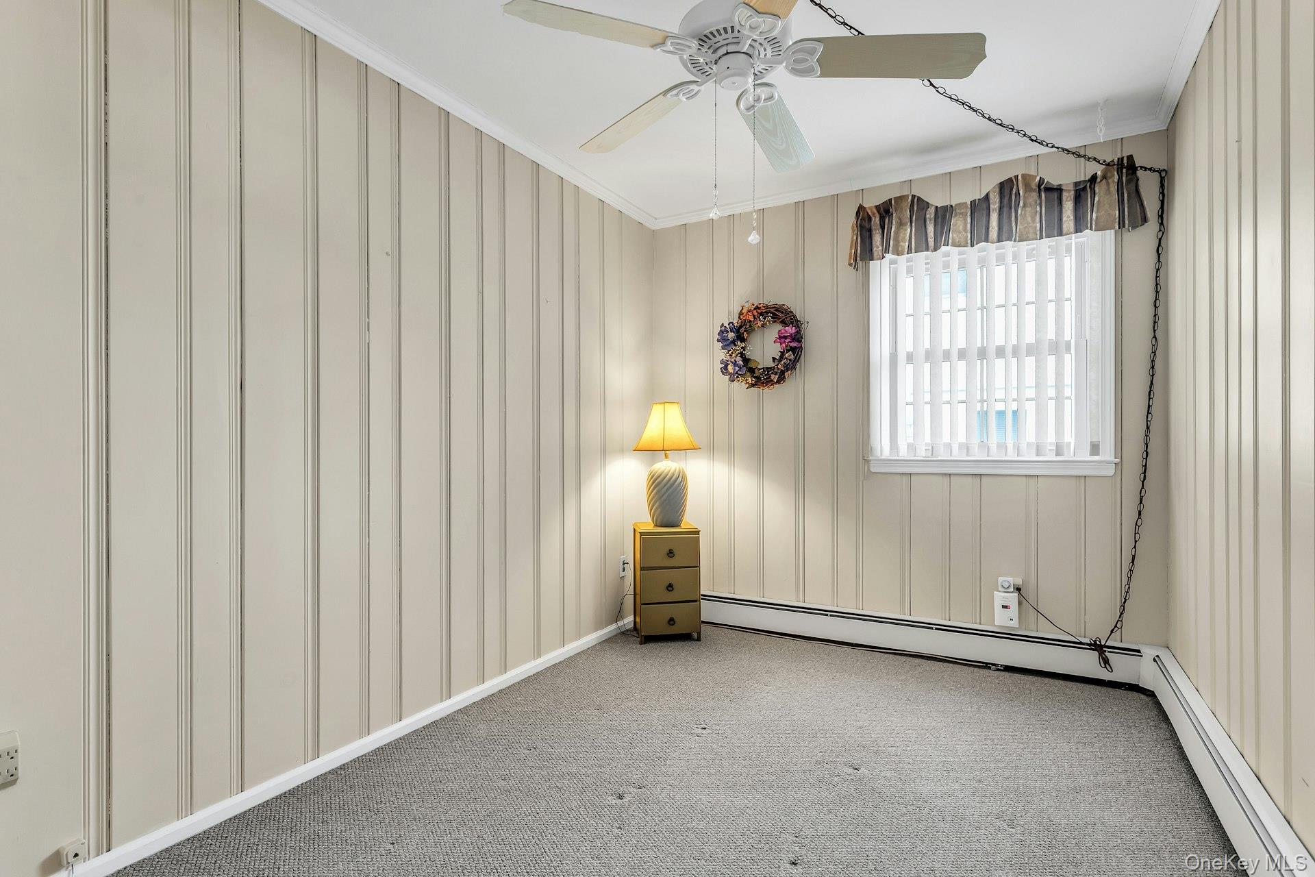 5 Sherwood Road Glen Cove, NY 11542 - Photo 12 of 26 Spare room featuring baseboard heating, crown molding, ceiling fan, and carpet floors