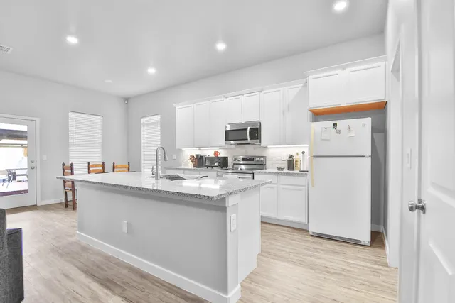 a kitchen with stainless steel appliances granite countertop a refrigerator a stove top oven a sink dishwasher and white cabinets with wooden floor