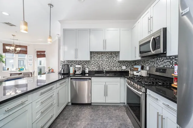 a kitchen with stainless steel appliances granite countertop a sink a stove a microwave oven a refrigerator with white cabinets and a wooden floor