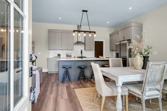 a dining room kitchen with stainless steel appliances kitchen island granite countertop a dining table chairs and a refrigerator