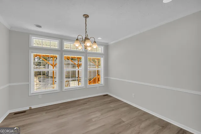a view of an empty room with chandelier and wooden floor
