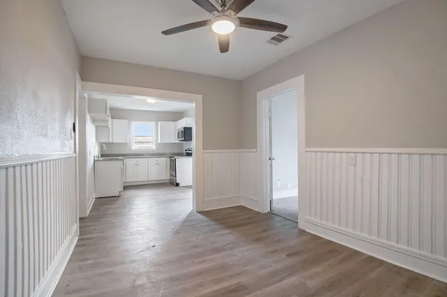 an empty room with wooden floor a ceiling fan and kitchen view