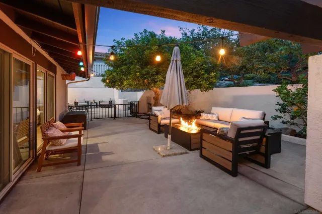 a view of a patio with couches table and chairs under an umbrella with a small yard