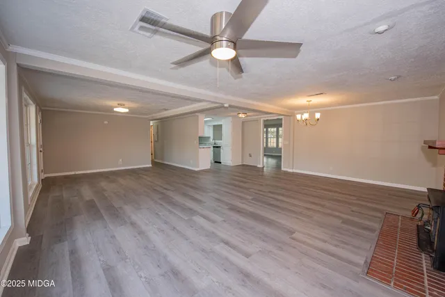 a view of an empty room with wooden floor and a ceiling fan