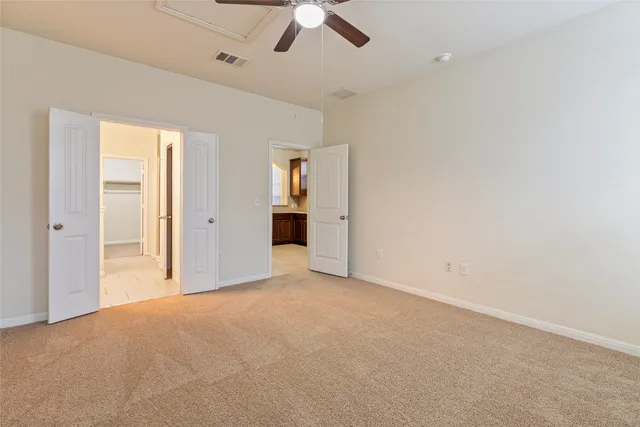 an empty room with chandelier fan and kitchen view