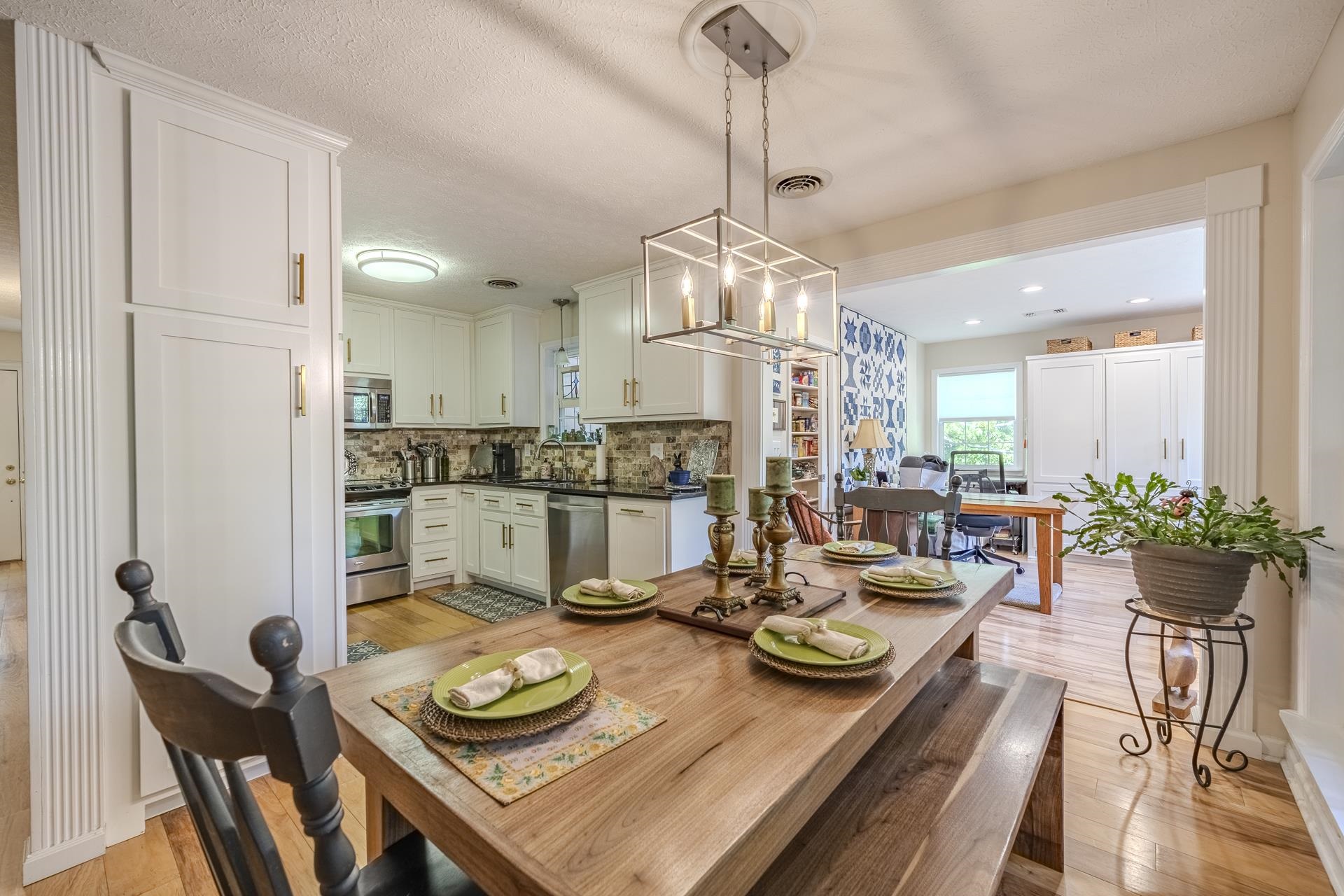 85 Cr 256 Road Iuka, MS 38852 - Photo 12 of 38 Open-concept dining area with wood-finish flooring, featuring a contemporary linear chandelier, white built-in cabinetry, and a clear sightline into the kitchen with stainless steel appliances