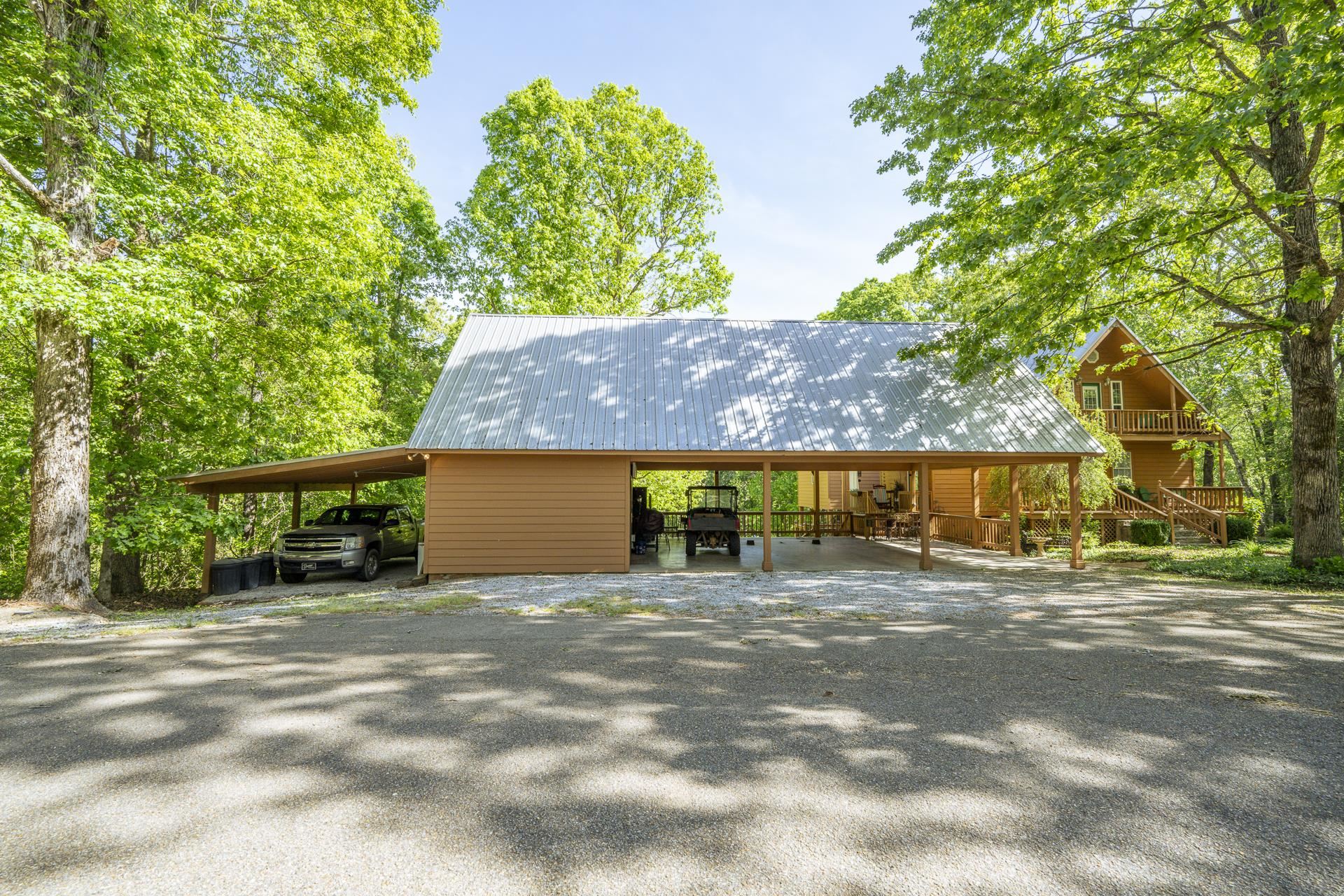 85 Cr 256 Road Iuka, MS 38852 - Photo 4 of 38 Expansive gravel drive with a carport structure featuring a corrugated metal roof and wood posts, complementing a distant A-frame style residence with a balcony and exterior staircase