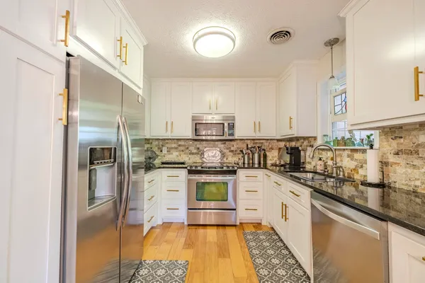 a kitchen with stainless steel appliances granite countertop a refrigerator a oven and white cabinets