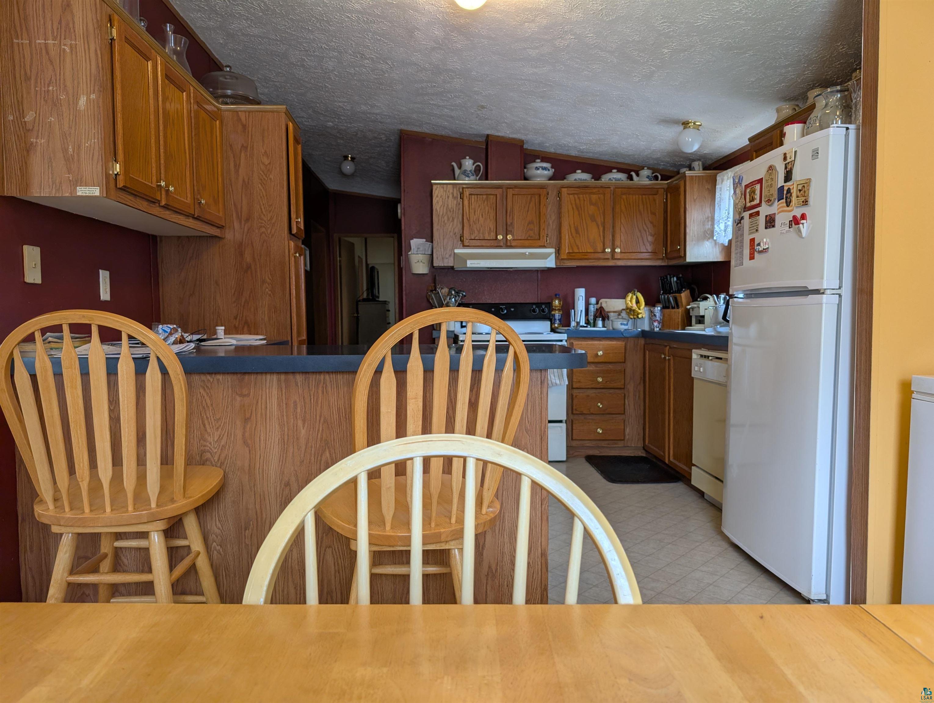 54700 Cudworth Avenue Grand View, WI 54839 - Photo 12 of 21 Kitchen with wood finish cabinets, dark countertops, white appliances, and a textured ceiling