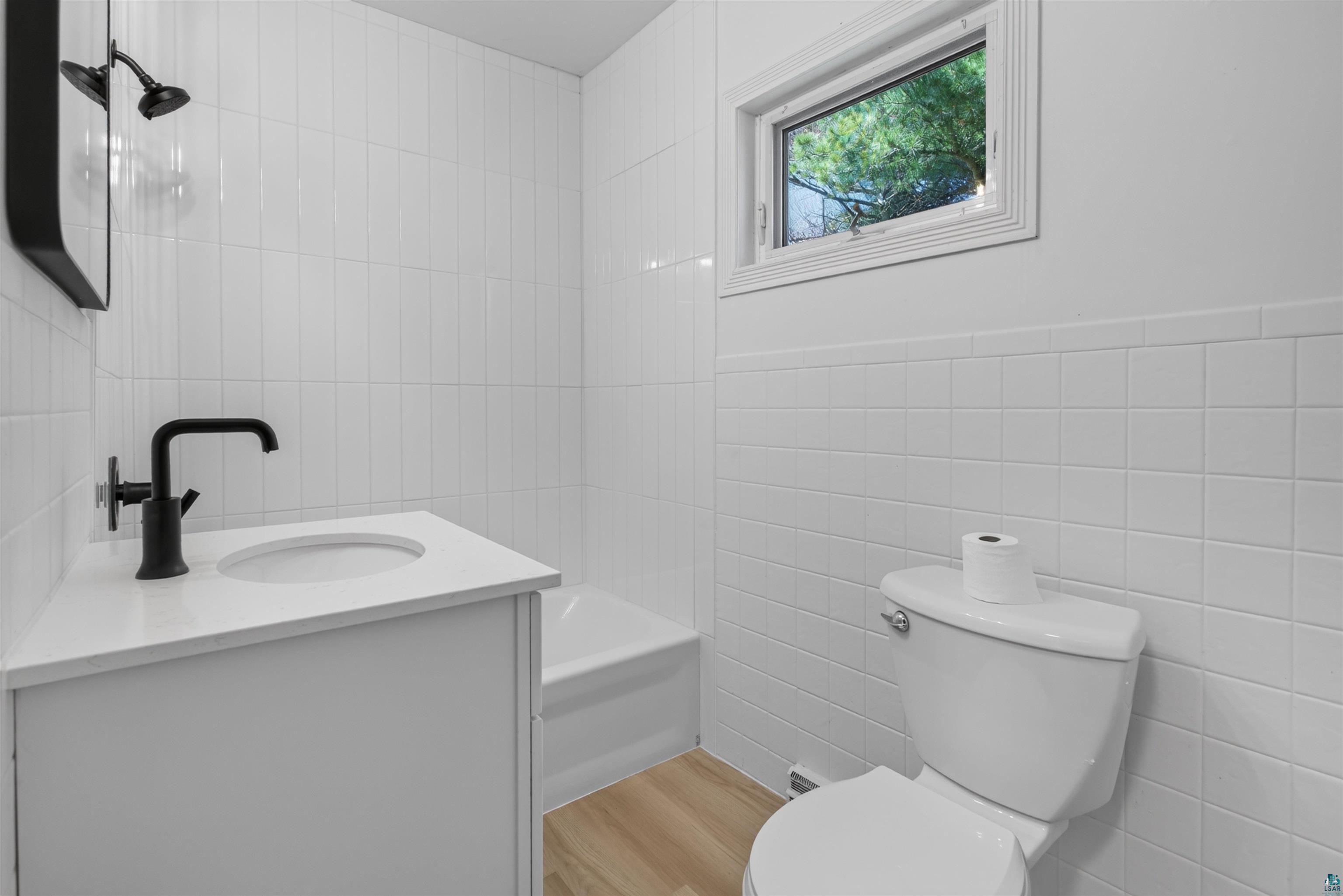 5868 Rice Lake Road Duluth, MN 55803 - Photo 27 of 39 Bathroom featuring white subway tile, a white vanity with a white countertop, a black faucet, and wood-finish flooring