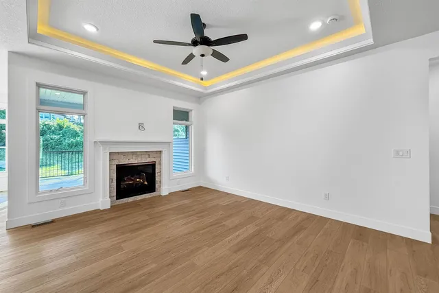 a view of a livingroom with a fireplace a ceiling fan and wooden floor
