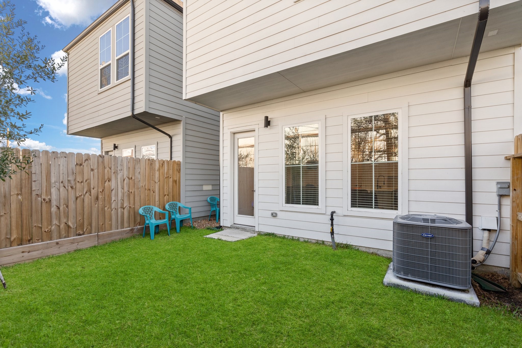 2928 Stevens Street Houston, TX 77026 - Photo 22 of 30 This image shows a small, fenced backyard with a neat grass lawn, adjacent to a two-story house with white siding. There's a patio area with three blue chairs and a visible air conditioning unit.