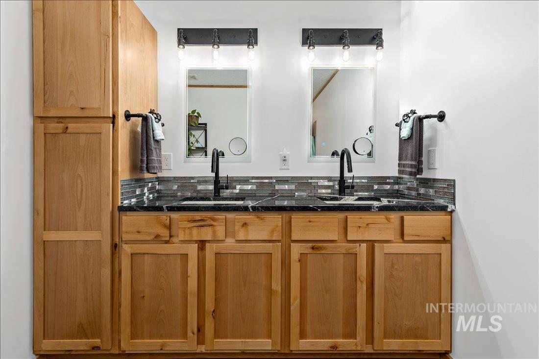 79 Sunset Loop Cascade, ID 83611 - Photo 24 of 44 Dual vanity featuring wood-finish cabinetry, black countertops, and a mosaic tile backsplash