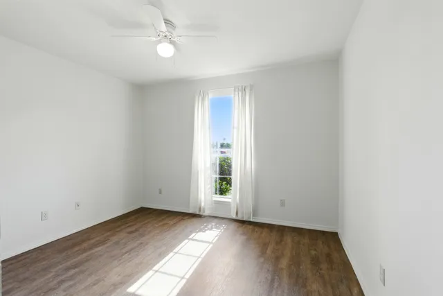 an empty room with wooden floor ceiling fan and windows