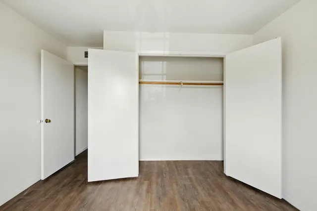 a view of an empty room with wooden floor and closet