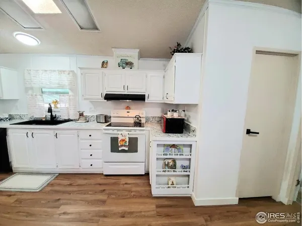 a kitchen with stainless steel appliances a stove a white refrigerator a sink and white cabinets with wooden floor