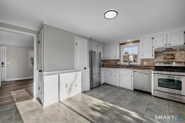 a kitchen with granite countertop a refrigerator oven a sink and white cabinets