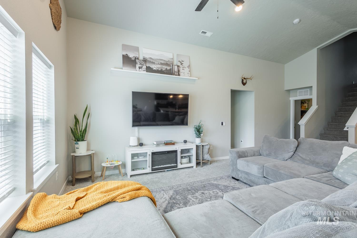12623 Shadow Peak Street Caldwell, ID 83607 - Photo 10 of 50 Spacious living area featuring light neutral wall tones, large windows with white blinds, and a built-in media console with an electric fireplace