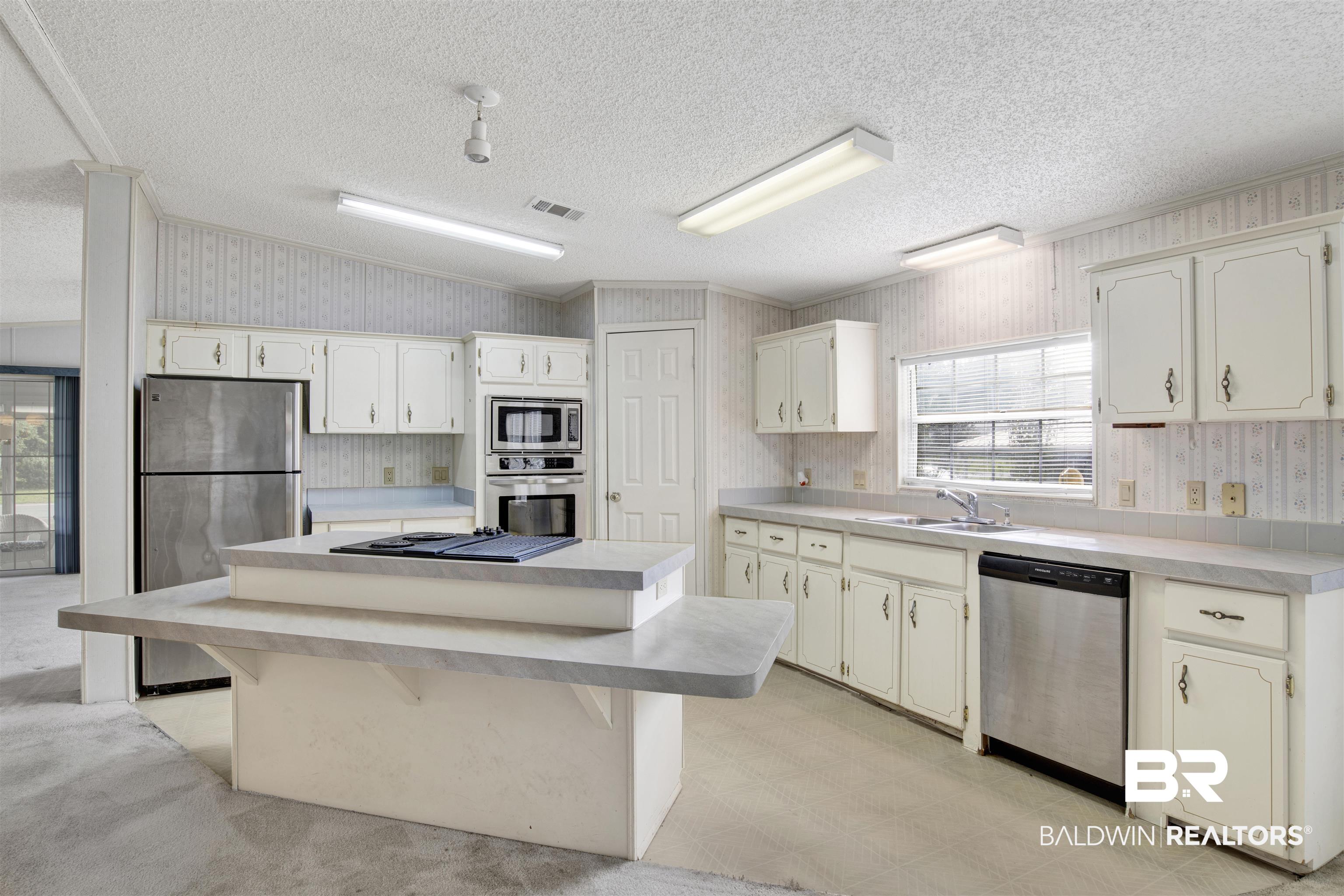 1216 Ridgewood Drive Lillian, AL 36549 - Photo 3 of 29 Kitchen with a kitchen breakfast bar, wallpapered walls, light countertops, a kitchen island, and stainless steel appliances