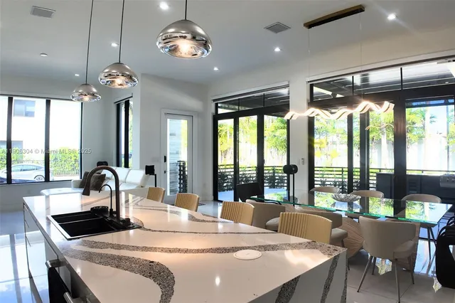 a kitchen with stainless steel appliances kitchen island granite countertop a stove a sink a dining table and chairs with large windows