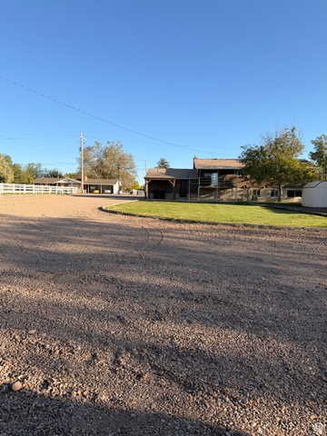 2298 West 800 North Clinton, UT 84015 - Photo 51 of 53 Expansive gravel driveway leading to a multi-structure property featuring a white picket fence, a dedicated grassy area, and mature trees