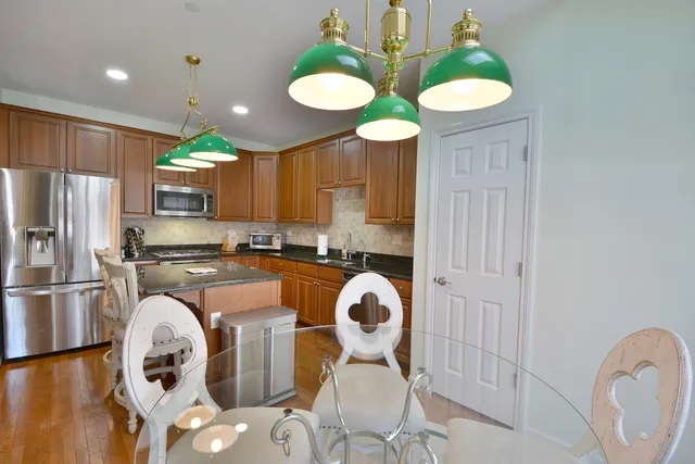 a kitchen with stainless steel appliances granite countertop a refrigerator a stove a sink and a dining table with wooden floor