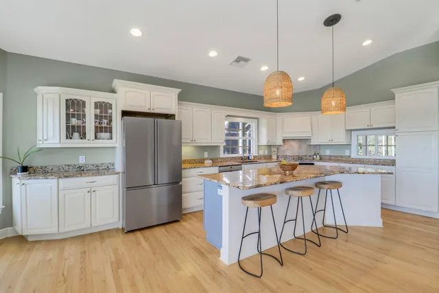 a kitchen with stainless steel appliances granite countertop a stove a refrigerator a sink dishwasher and a dining table with wooden floor