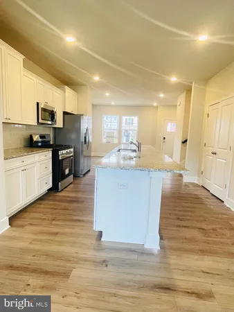 a large white kitchen with kitchen island a sink wooden floor and stainless steel appliances