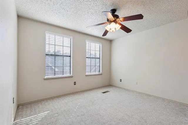 an empty room with chandelier fan and windows