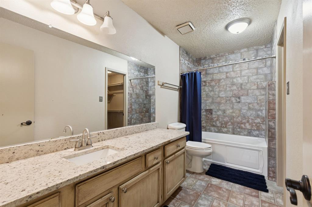 449 Harris Street, Unit 103B Coppell, TX 75019 - Photo 23 of 26 a bathroom with a granite countertop sink a toilet a mirror and bathtub