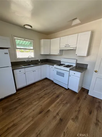 a kitchen with stainless steel appliances granite countertop a stove a sink white cabinets and a wooden floors