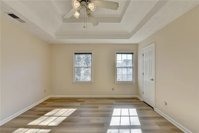 an empty room with wooden floor chandelier fan and windows