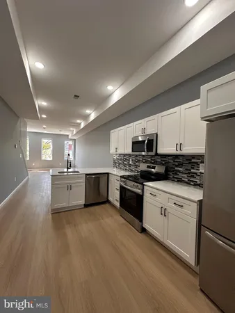 a large white kitchen with stainless steel appliances granite countertop a stove a sink a refrigerator and white cabinets with wooden floor