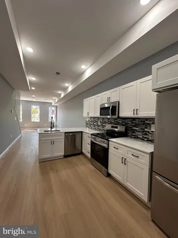 a large white kitchen with stainless steel appliances granite countertop a stove a sink a refrigerator and white cabinets with wooden floor