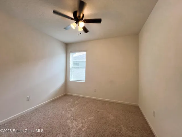 an empty room with a chandelier fan and windows