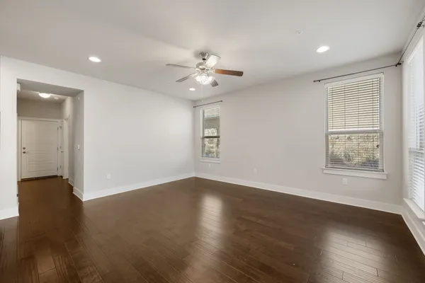 an empty room with wooden floor chandelier fan and windows