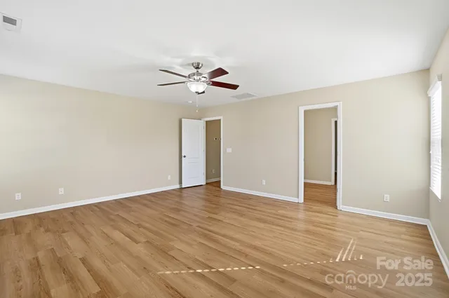 a view of an empty room with wooden floor and a ceiling fan