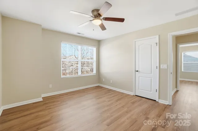 an empty room with wooden floor chandelier fan and windows