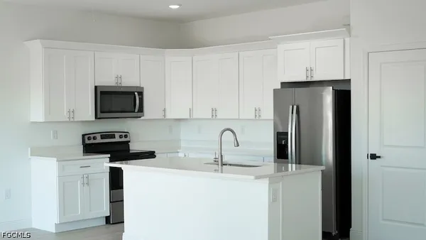 a kitchen with stainless steel appliances a refrigerator a sink a stove top oven and white cabinets